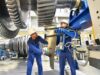 2 Werksarbeiter bauen eine große Turbine zusammen